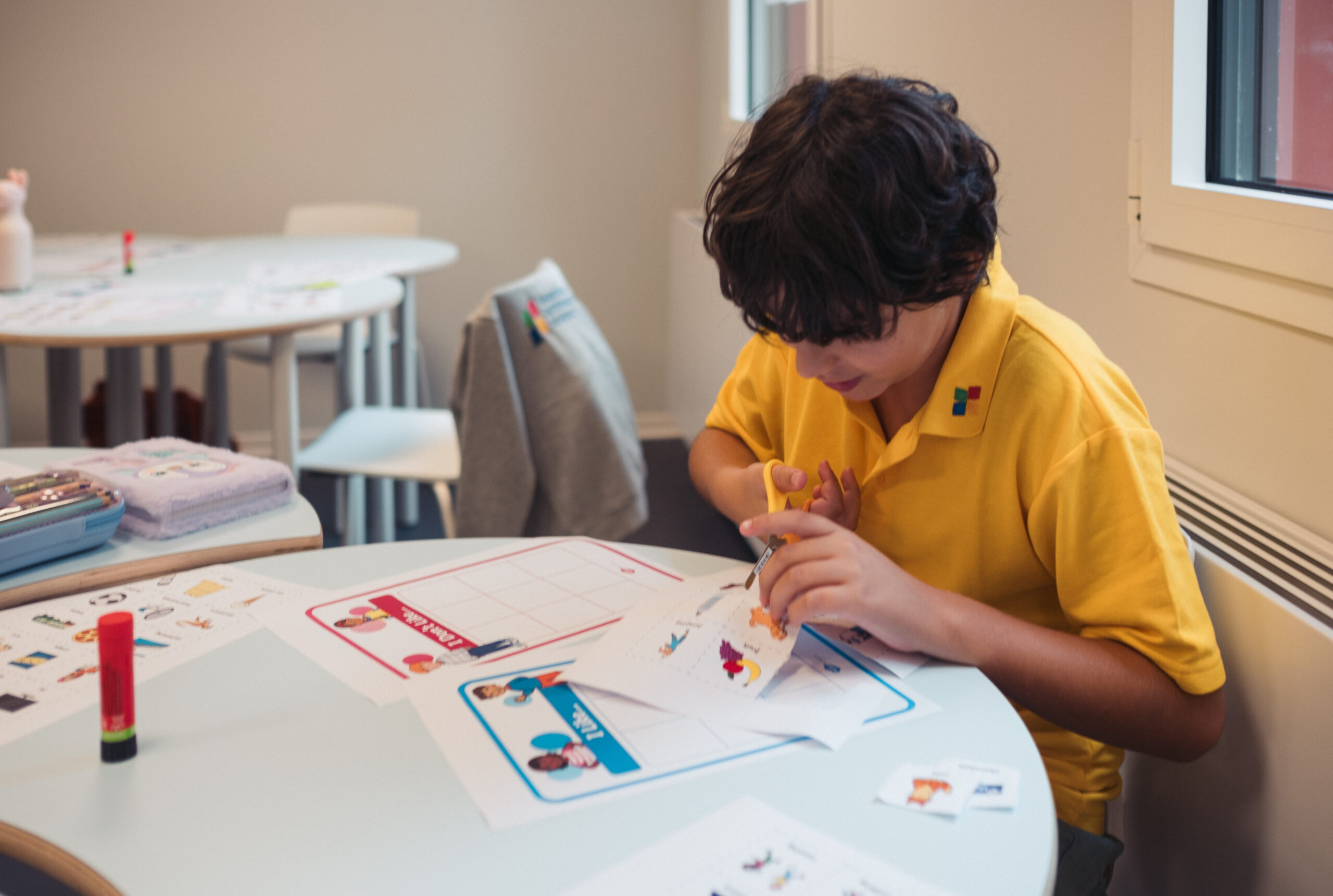 A child sits at a school desk, carefully cutting out a paper craft during an arts and crafts activity.