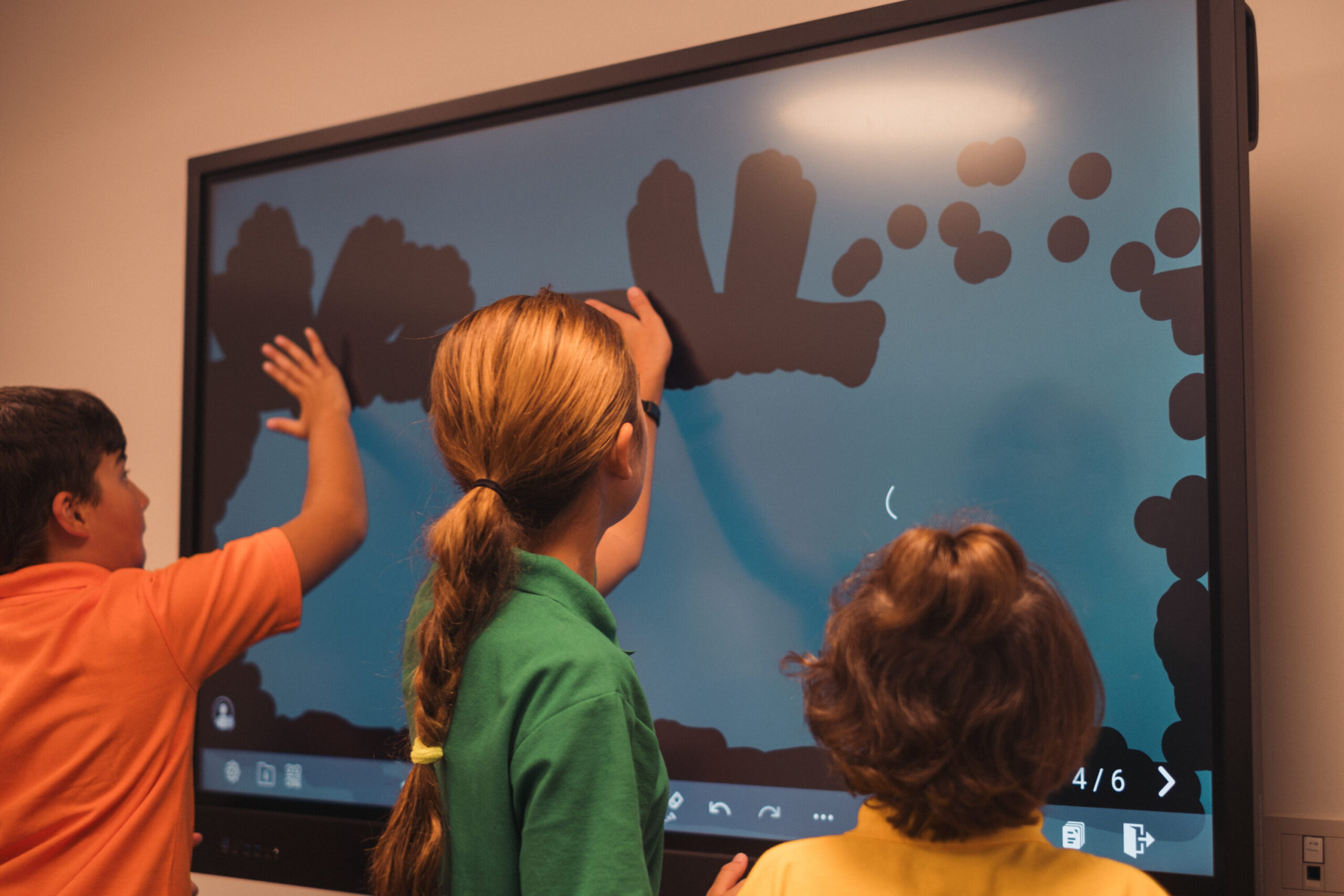 Children gather around a desk at Sardinia International School, engaging with enthusiasm as they explore how to use it together in a classroom setting.
