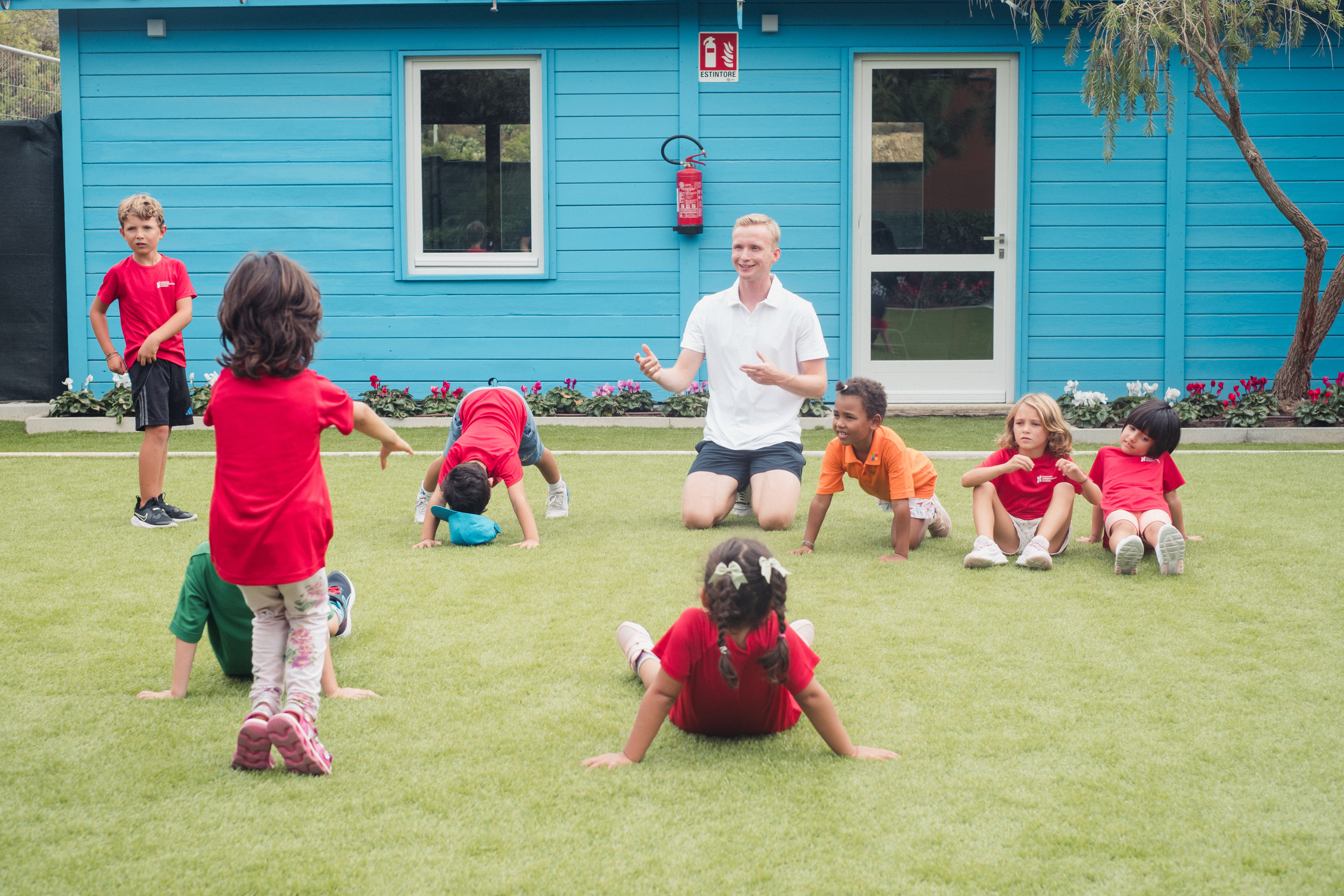 Teacher and young children playing ball on the grass at Sardinia International School